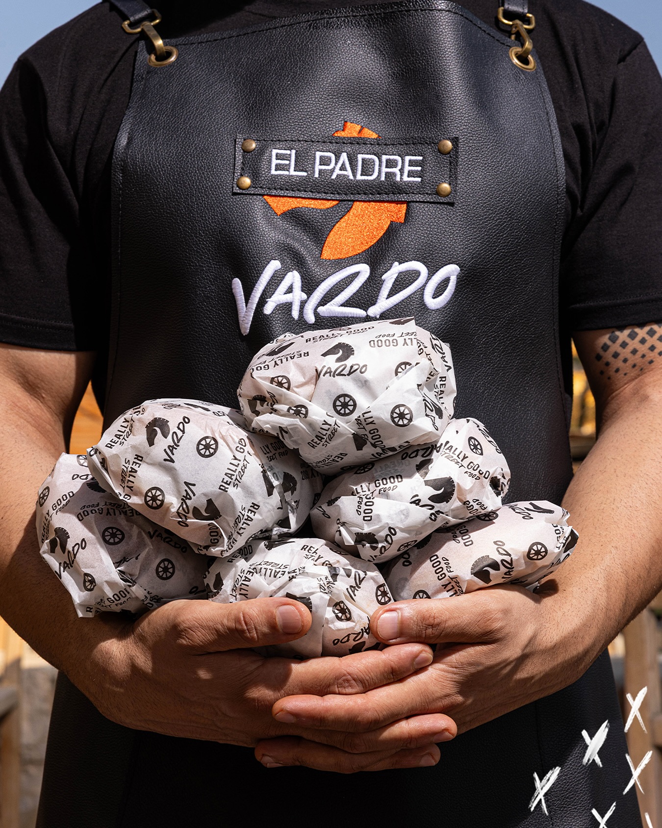 A Vardo cook holding an armful of paper-wrapped burgers